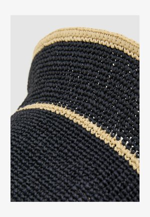 Detailný záber na čierny slamený klobúk s béžovým opleteným lemom pozdĺž okraja a čelenky na korunke.