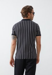 Polo shirt rayé noir à manches courtes, featuring des lignes verticales blanches. Fabriqué en tissu doux, avec un col classique et une coupe ajustée.