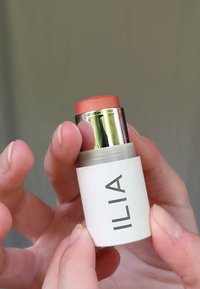 ILIA cream blush stick i ett vitt behållare med ett silver- och persikofärgat lock. Produkten har en slät konsistens och en varm korallfärg.