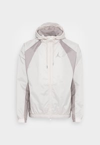 Vit vindjacka med grå detaljer, dragkedja fram, justerbar huva, elastiska ärmslut och midja, med en liten logotyp på bröstet.