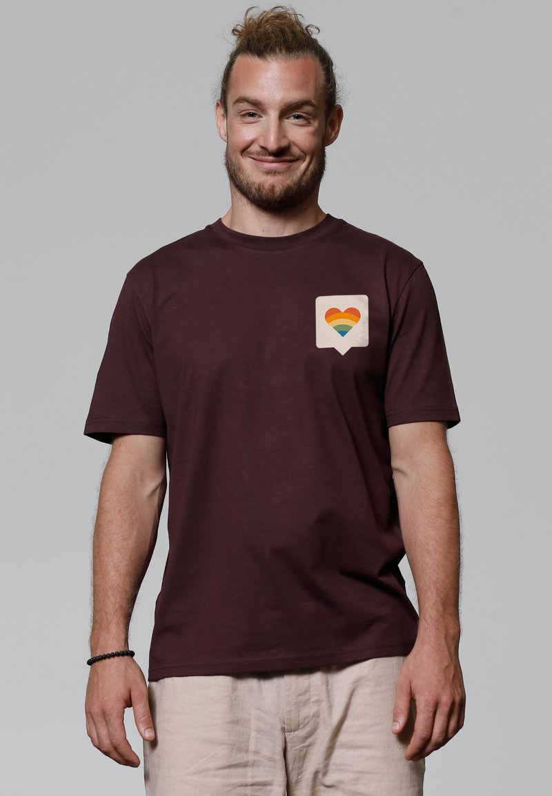 T-shirt en coton bordeaux à manches courtes et col rond, arborant une icône de cœur multicolore sur une bulle de dialogue blanche sur la poitrine.