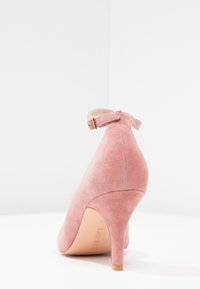 Rosa mockaskinn högklackad sko med rund tå och ankelrem, med en smal klack och slät yta, visad bakifrån.