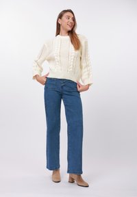 Off-white strikket sweater med et tekstureret mønster, kombineret med højtaljede blå denimjeans og beige ankelstøvler.