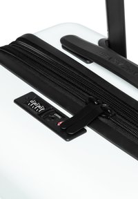 Valigia rigida bianca con zip e accessori neri, dotata di una combinazione di lucchetto e maniglia liscia, progettata per la comodità durante i viaggi.