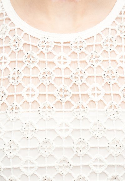 Tissu blanc transparent avec motif géométrique en crochet en forme de losange, orné de perles autour d'un col rond.