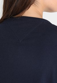 Navy blue cotton t-shirt featuring a rounded neckline, short sleeves, and a triangular stitch detail at the back neck. Smooth texture.