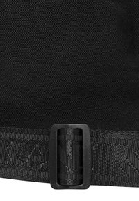 Borsa nera in tessuto con superficie testurizzata, dotata di una fibbia nera liscia e di una tracolla coordinata a motivo lungo il bordo inferiore.