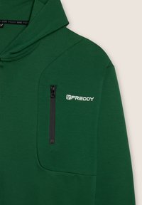 Sudadera verde con un bolsillo de pecho con cremallera, textura suave, capucha ajustable con cordón y el logo "FREDDY" en blanco en el lado izquierdo.