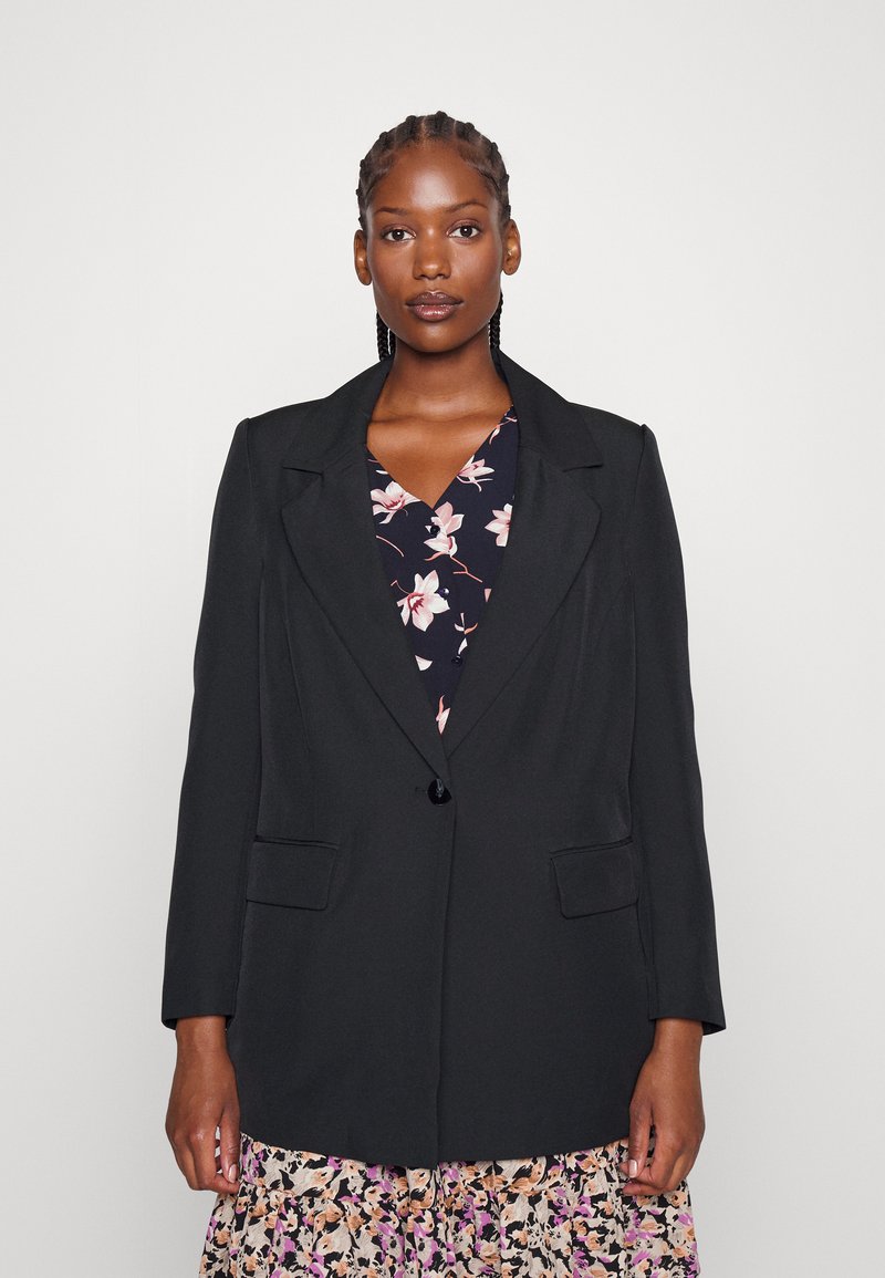 Black blazer with a notched lapel, single button closure, and two front pockets, worn over a floral patterned dress.