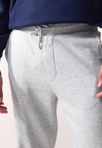 Graue Sweatpants mit einem Kordelzugbund, seitlichen Taschen und weichem, strukturiertem Stoff. Sie haben eine lässige Passform und ein schmal zulaufendes Bein-Design.