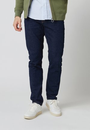 Donkerblauwe denim jeans met een slim fit. Gecombineerd met een lichtblauw gestreept shirt en witte sneakers, met een minimalistisch ontwerp.