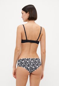 Svart behå med justerbara axelband och krokstängning, i kombination med vita bikiniunderdelar med ett svart abstrakt mönster.