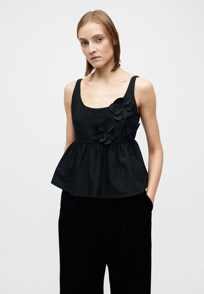 Svart ermeløs topp med tettsittende liv og utflaret peplum. Har tre stoffblomster på venstre side. Laget av glatt, lett materiale.