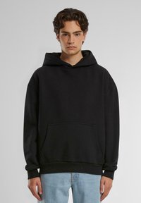 Sort hættetrøje lavet af blødt stof, med en frontlomme, løs pasform og ribbede manchetter. Båret med lyseblå jeans.
