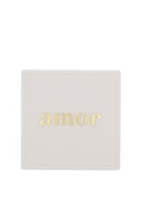 Kvadratisk, mjukt ljusrosa yta med präglad kant. Ordet "amor" i feta, glänsande guldbokstäver centrerat på framsidan.