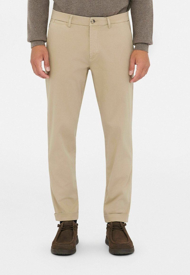 Pantalones de algodón beige con corte recto, bolsillos frontales y cierre de un solo botón, combinados con zapatos de ante marrón.