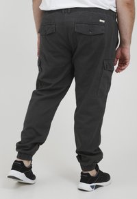 Graue Cargo-Hosen mit elastischen Bündchen, zwei Gesäßtaschen mit Knöpfen und seitlichen Taschen. Das Material wirkt strapazierfähig und hat eine glatte Textur.