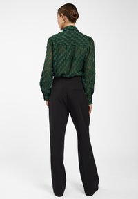 Groene doorschijnende blouse met een textuur en geweven patroon, gecombineerd met zwarte hoge taille broeken met een rechte pijpdesign.