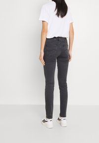 Vaqueros negros de corte ajustado con cintura alta, dos bolsillos traseros y detalles mínimos en las costuras. Combinados con zapatillas blancas.