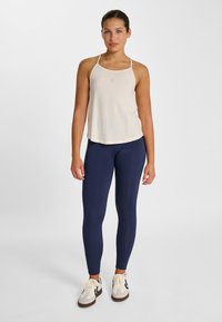 Light beige tank top with thin straps, paired with navy blue leggings, and white sneakers with grey accents and black stripes.