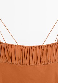 Top color ruggine con scollatura elastica arricciata e sottili spalline regolabili. Tessuto liscio con un design semplice e lineare.