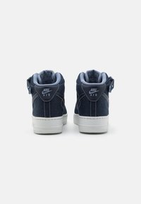 Tenisky Nike Air s denimovým svrškem v tmavě modré barvě, polstrovaným límcem, bílou gumovou podrážkou, logem na zadní straně a texturovanými detaily.