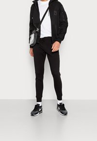 Svart zip-up hoodie med sidfickor, i kombination med svarta tapered sweatpants och svarta sneakers. Vit t-shirt och en liten crossbody-väska.