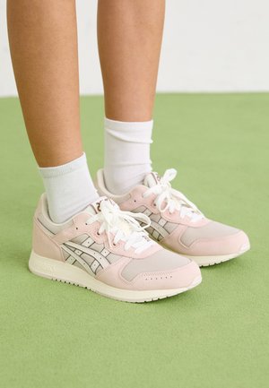 Lichtroze sportschoenen van mesh en suede materialen, met witte veters, zilveren accenten en een gestructureerde zool. Witte enkelsokken zichtbaar.