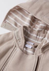 Beige Fleecejacke mit gestreifter Innenausstattung, ausgestattet mit einem Vorderreißverschluss und Druckknöpfen am Kragen; weicher Stoff und schlichtes Design.
