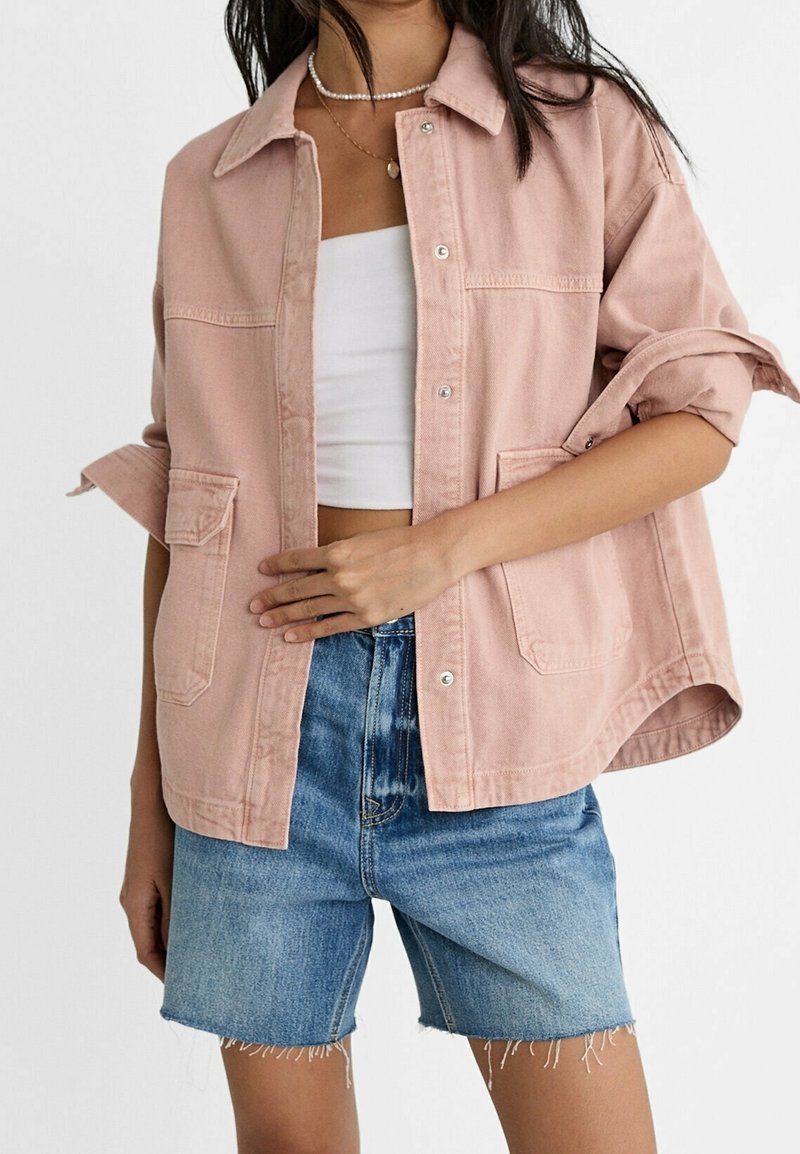 Giacca in denim rosa chiaro con vestibilità comoda, due tasche frontali e maniche risvoltate, abbinata a pantaloncini in denim blu. Tessuto morbido.