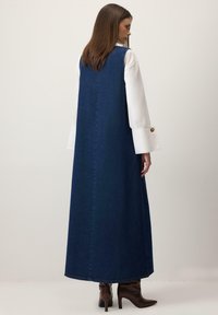 Tumši zilas džinsa maksi kleita ar taisnu griezumu. Vienkāršs dizains, sānu šķēlumi un viegla tekstūra; sader ar brūniem zābakiem ar papēdi.