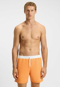 Heren zwemshorts in fel oranje met een witte elastische tailleband en trekkoord. Glad van textuur, knielang, met zijzakken.