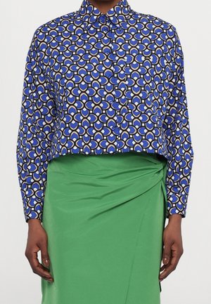 Niebieska, czarna i beżowa koszula z długim rękawem, zapinana na guziki, z geometrycznym wzorem, w połączeniu z zieloną spódnicą kopertową z wysokim stanem.