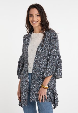 Kimono floreale con maniche lunghe, realizzato in tessuto leggero di colore blu scuro, decorato con piccoli fiori blu e rosa. Indossato sopra una maglietta bianca.