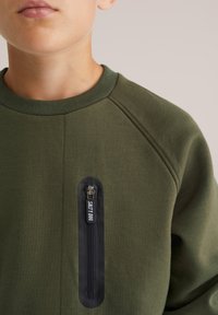 Olivazöld pulóver, kerek nyakkivágással és raglánujjakkal, cipzáras zsebbel, fekete díszítéssel és "SALTY DOG" felirattal.