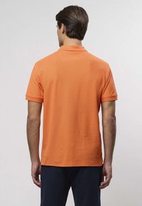 Oranžidest triiksärgist polo, valmistatud puuvillast, millel on lühikesed varrukad ja klassikaline krae. Disain on lihtne, sileda tekstuuriga ja ilma mustriteta.