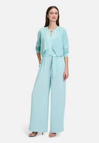 Ljusblå overall med vida ben och ett knytbälte, tillsammans med en matchande öppen cardigan. Mjuk, slät tyg med en strukturerad halsringning.