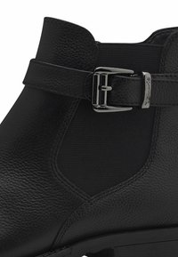 Botín negro de cuero con un acabado texturizado, paneles laterales elásticos y un acento de hebilla plateada en la correa.