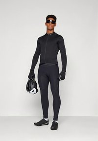 Juoda dviračių apranga su ilgomis rankovėmis, priekyje užtrauktuku ir su paminkšlintomis kelnėmis. Priedai: juodos pirštinės ir baltas su juodu šalmas.