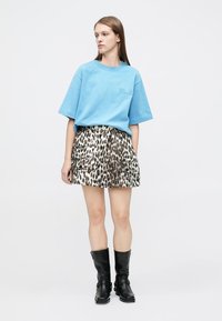 T-shirt oversize bleu clair à manches courtes, associée à une jupe à volants imprimée léopard. Des bottes noires montantes complètent la tenue.