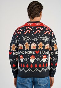 Svart och röd festlig stickad tröja med motiv av godiskäppar, snöflingor, pepparkaksgubbar, hus och jultomte, med ribbade ärmslut och nederkant.