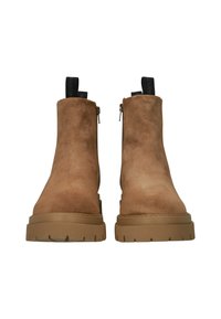 Botas de tobillo de ante en marrón claro con una suela de goma gruesa y texturizada. Cuenta con un cierre de cremallera y una lengüeta para ponérselas fácilmente.