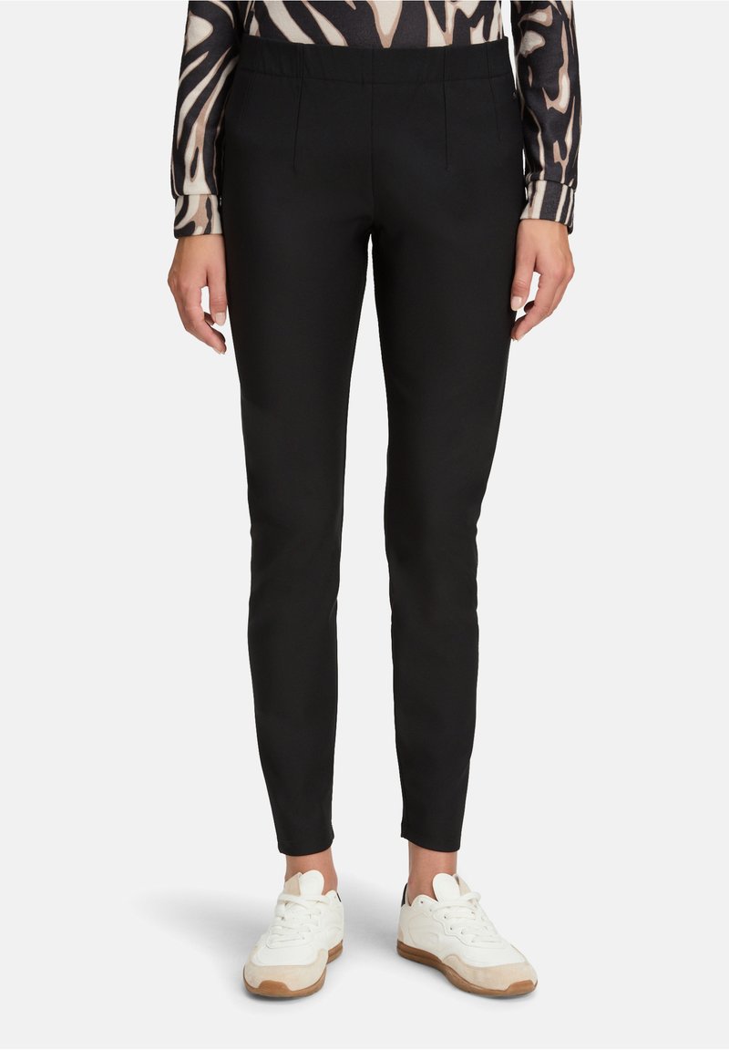 Czarne, dopasowane spodnie o gładkiej tkaninie, z korzystnym fasonem pasa i dwoma przednimi kieszeniami. W połączeniu z białymi i beżowymi sneakersami.