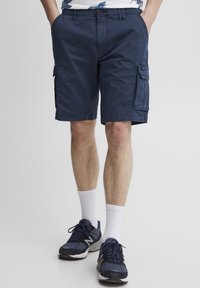 Pantaloni scurți cargo de culoare albastră marin�ă, cu multiple buzunare, realizati dintr-un material ușor. Prezintă o croială lejeră și un design de lungime până la genunchi, asortați cu șosete albe și încălțăminte.