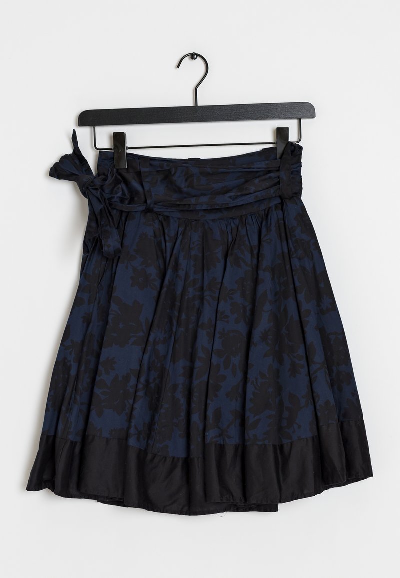Jupe marine avec un motif floral, tissu texturé, plis froncés et ourlet noir. Présente un lien sur le côté à la taille. Accrochée à un cintre noir.