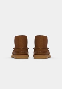 Brown leather ankle boots with a stitched seam detail, rounded toe, and flat rubber sole, showing a smooth, matte texture.