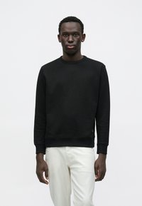 Μαύρο φούτερ με ριμπ λαιμόκοψη και μανσέτες, με υφή υφάσματος και άνετη εφαρμογή. Συνδυάζεται με λευκό παντελόνι.