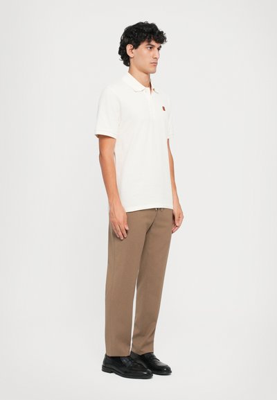 Lys beige polo skjorte med korte ærmer, krave og et lille broderet logo. Sæt sammen med tapered brune bukser og sorte sko.