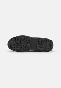 Black rubber shoe sole with intricate leaf and flame patterns, flat design and textured surface for grip. Circular logo detail at the heel.