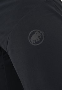 Svarta utomhusbukser i lätt material, med en slät yta och en subtil logotyp av en elefant i en cirkulär design.